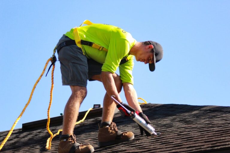 A homeowner uses a ladder to visually inspect the edge of a tiled roof under bright, partly cloudy skies.