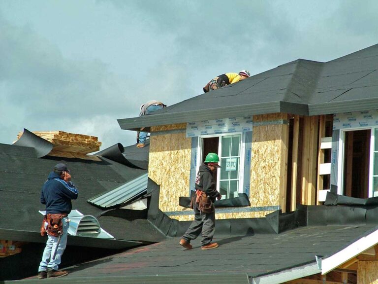 A roofing inspector examining shingles with a clipboard and ladder visible against a residential roof.